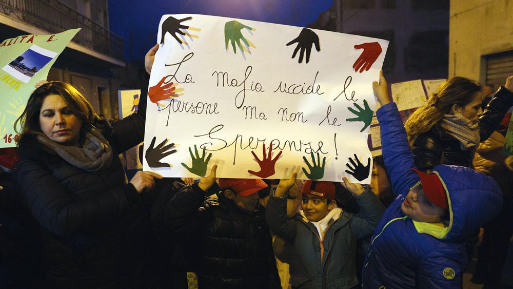 Bild: Erwachsene und Kinder bei einer Demonstration halten ein Plakat mit bunten Handabdrücken und der italienischen Aufschrift ‚La mafia uccide le persone ma non le speranze!‘