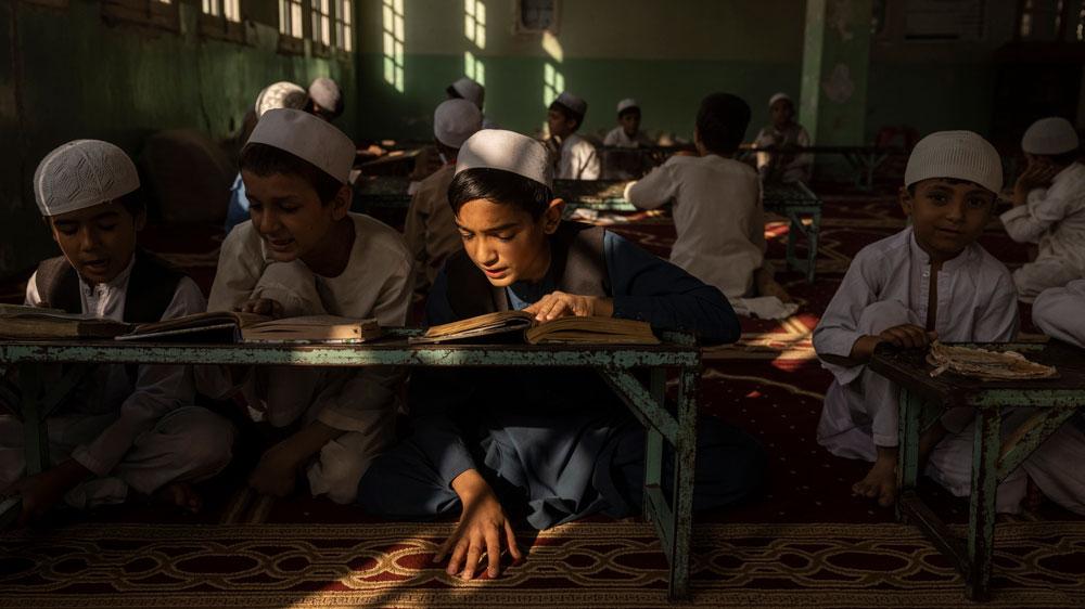 Bild: Ein Junge sitzt in einem Lichtstrahl in einem ansonsten schattigen Raum in deiner von den Taliban geleiteten Madrasa