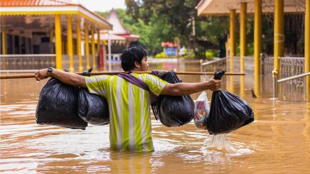 Bild: Ein Mann trägt seine Habe in zwei Platiktüten durch hüfthohes Wasser während einer Flutkatasrophe in Thailand, September 2021