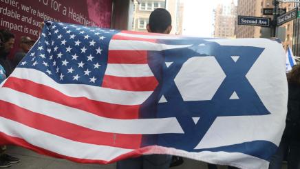 Bild: Ein Demonstrant hält eine Fahne, in der die Flaggen der USA und Israels miteinander verschmelzen