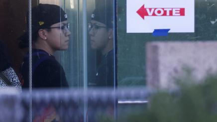 Ein Schild „Vote“, das den Weg zur Wahlkabine zeigt, dahinter eine Person